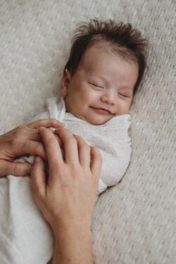 A tiny newborn lays sleeping in his mother's hands with a sweet little smile