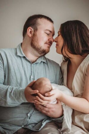 A couple press noses together lovingly as they hold their newborn baby