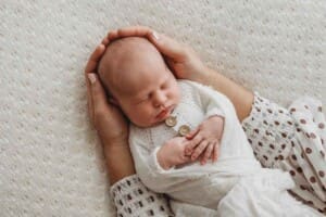 A mothers hands gently hold her sleeping newborn baby wrapped in a white blanket