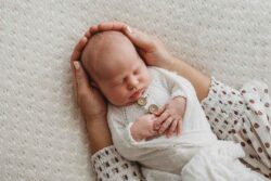 A mothers hands gently hold her sleeping newborn baby wrapped in a white blanket