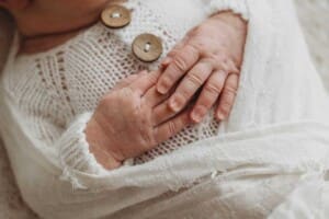 A detail image of a newborn baby's hands folded over her in a white cloth wrap