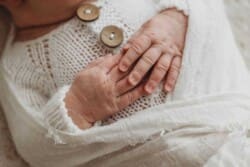 A detail image of a newborn baby's hands folded over her in a white cloth wrap