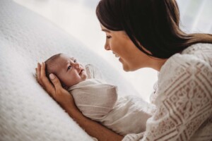 A mother holds her newborn baby in her hands as she lays wrapped on a white blanket