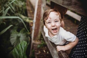 A little boy pokes his head through the railing on a boardwalk and giggles during his family session