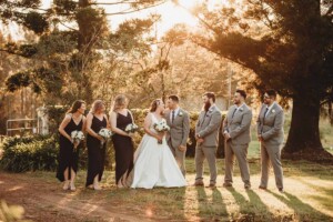 A bridal party stand amongst trees at sunset during their Gledswood Estate wedding