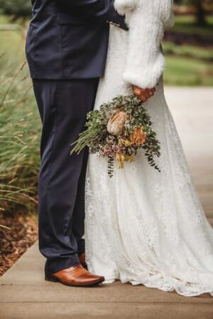 A brides colourful bouquet hangs by her side as she hugs her groom