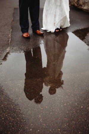 A bride and groom stand next to a puddle where their reflections are shown