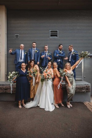 A bridal party stand together against a grey warehouse door and celebrate after the wedding ceremony
