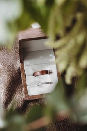 A couples wedding rings surrounded by the greenery of the brides bouquet
