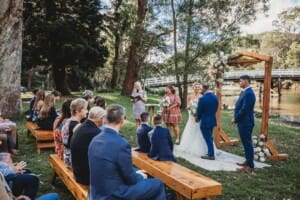 Guests sit on wooden benches watching the bride and groom during a wedding ceremony at Audley