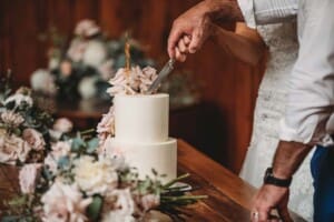 A close up of a bride and groom's hands as they cut their wedding cake