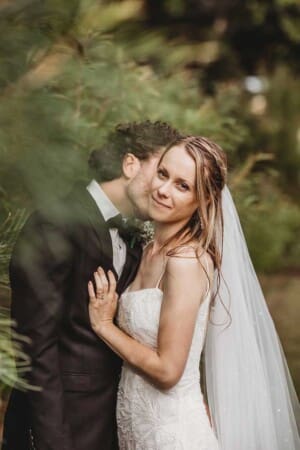 A groom kisses his bride on her cheek as she looks away and cuddles close to him