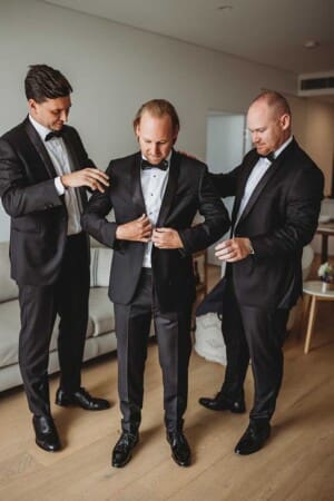 A groom and his groomsmen get dresses into black suits and ties as they get prepared for the wedding