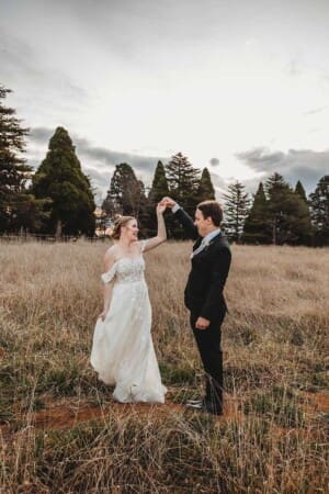 A groom dances with his bride in a grassy field at Bendooley with the sunset behind them