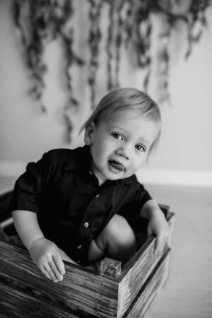A little boy sitting in a timber crate sticks his tongue out in a cheeky grin