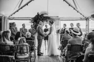 A couple stand under a marque surrounded by guests at their wedding ceremony
