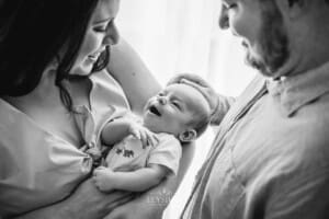 Parents hold their newborn baby between them as he smiles