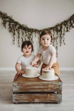 Twin boys sit beside a wooden crate and smash their first birthday cakes