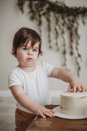 A baby boy sits beside a wood crate and smashes his first birthday cake