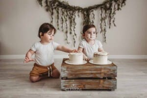 Twin boys sit beside a wood crate and smash their first birthday cakes