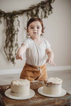 A baby boy with a face covered in cake smiles during his cake smash session