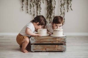Twin boys sit beside a wood crate and devour their first birthday cakes