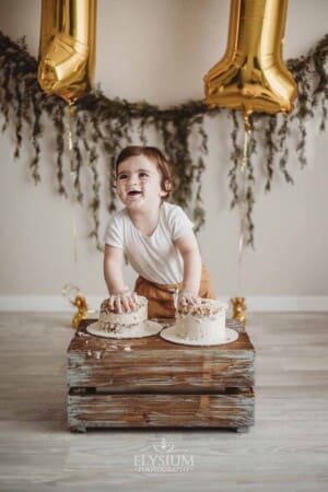 A baby boy giggles as he smashes his birthday cake which sits on a wooden crate