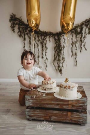 A baby boy giggles as he smashes his birthday cake which sits on a wood crate