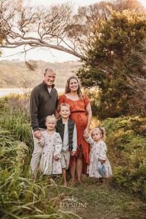 A family of 5 stand in a green leafy area at sunset