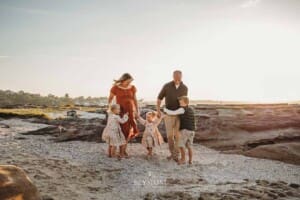 A family of 5 play together on a sandy beach at sunset