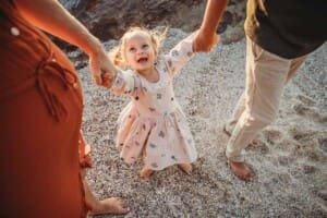 A little girl grins up at her parents as they swing her between them on a beach