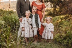 Three children stand in front of their parents surrounded by lush bushes