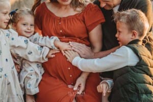 A pregnant woman sits with her family as her children place their hands on her belly