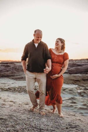 A couple walk hand in hand on a beach at sunset