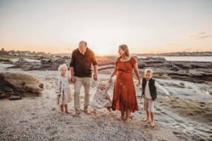 A family of 5 swing their youngest between them as they walk along a sandy beach