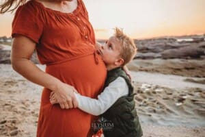 A boy gazes up at his pregnant mum and cuddles her belly at sunset