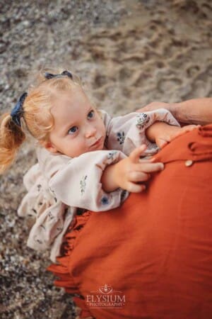 A little girl reaches up to cuddle her pregnant mum's belly
