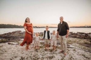 A pregnant mother stands on a sandy beach with her family at sunset