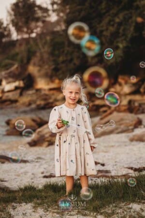 A little girl holds a bubble wand and blows bubbles on a sandy beach