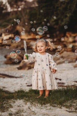 A little girl holds a bubble wand and blows bubbles on a sandy beach