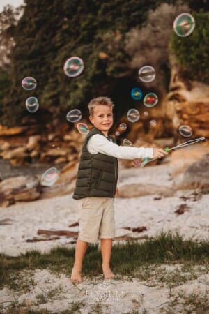A boy waves a bubble wand and blows bubbles on a sandy beach