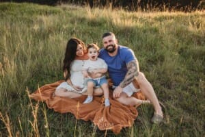 A pregnant mother sits on a blanket with her family in a grassy sunlit field