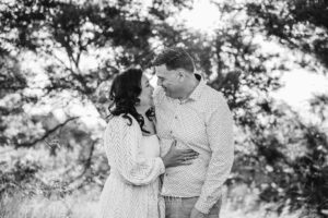 Parents embracing while standing in a bright field, enjoying a quiet and natural family photography moment at sunset