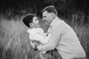 A father embraces his son in the long grass during a fun‑filled sunset session with their Ingleburn family photographer