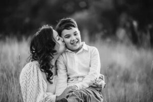 A mother kisses her son's cheek with long grass swaying around them, photographed at sunset in South West Sydney