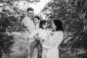 Family laughing together in the long grass during a fun‑filled sunset session with their South West Sydney family photographer