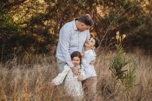 Children cuddled close to their parent as the sun sets behind them, a heartfelt outdoor family photography moment