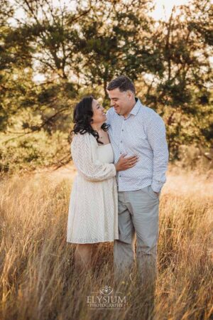 Parents embracing while standing long grass at sunset, enjoying a quiet and natural family photography moment