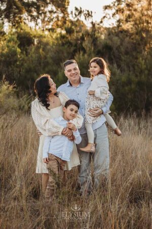 Family laughing together in the long grass during a fun‑filled sunset session with their South West Sydney family photographer