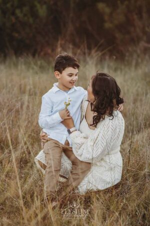 Little boy offering his mum a tiny wildflower with a proud smile, a sweet detail from their fun‑filled outdoor family session